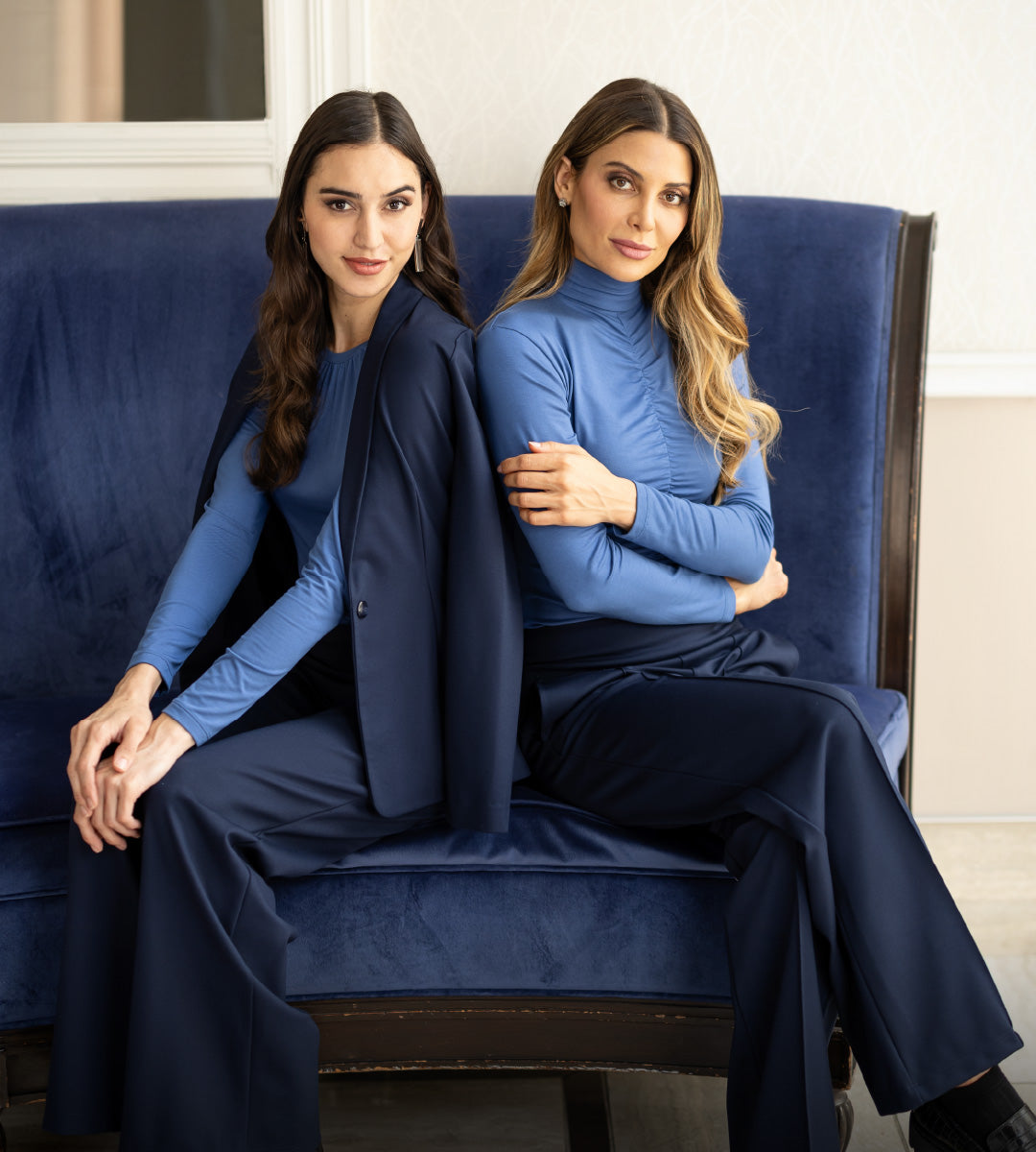 Two women sitting on a blue couch wearing blue outfits.