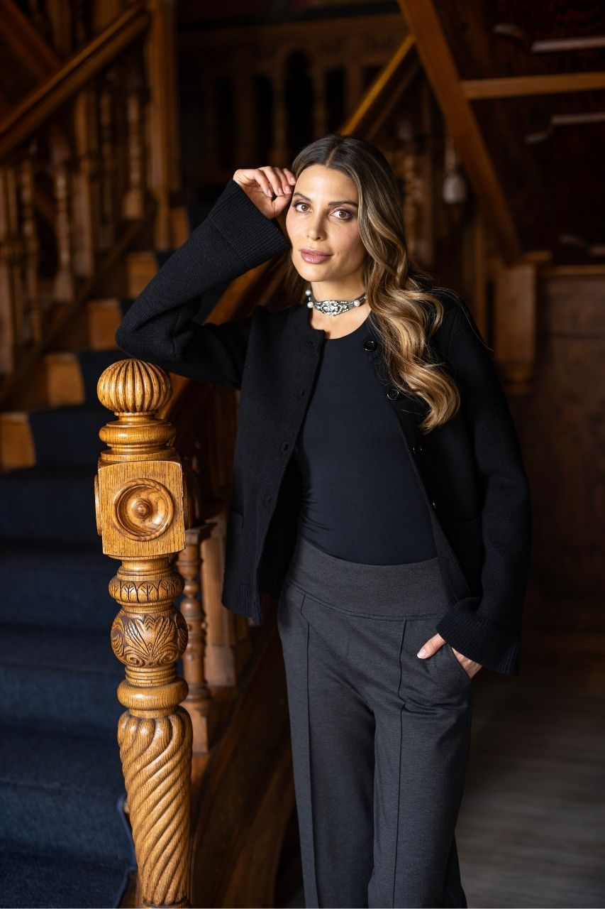 Woman in a black cardigan standing in a room with wooden staircase