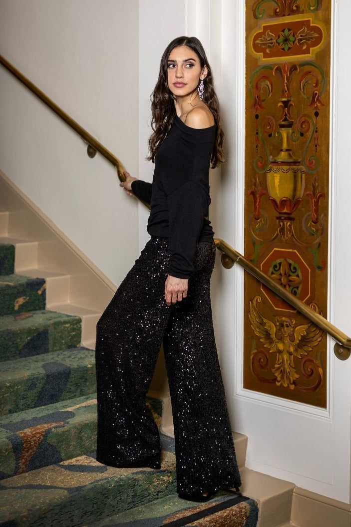 Woman in black outfit with sequin pants standing on a staircase with decorative wall art in the background