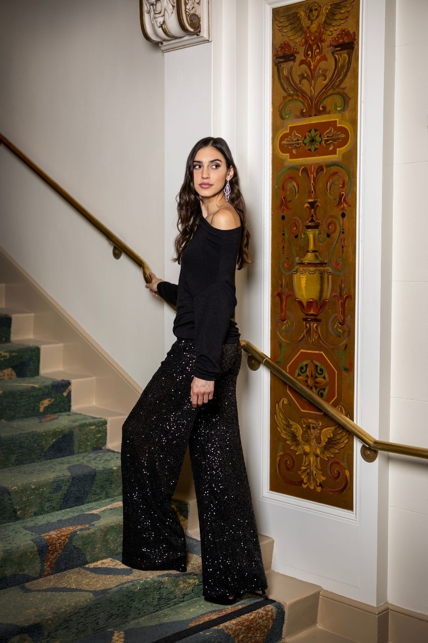Woman in black outfit with sequin pants standing on a staircase with decorative wall art in the background