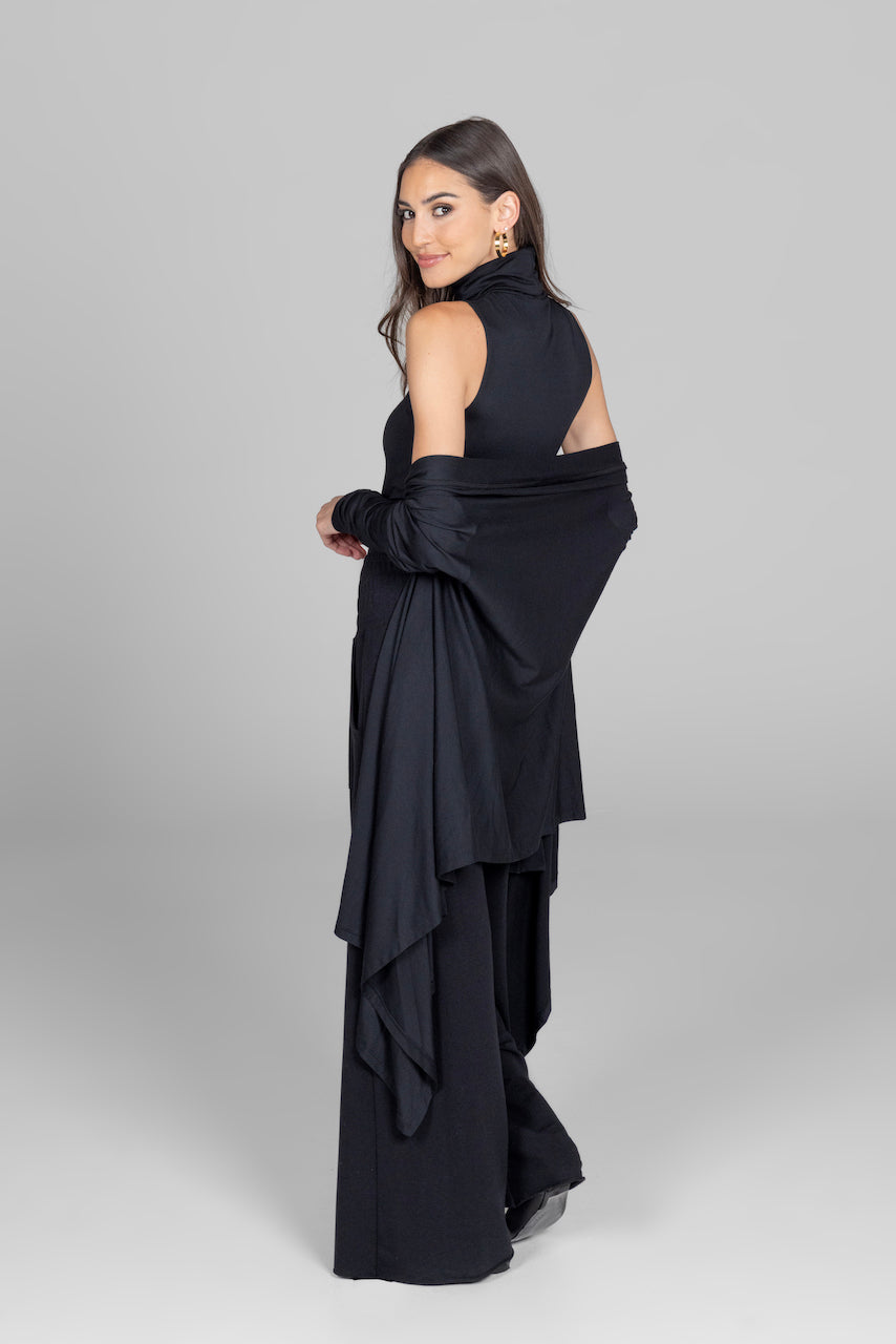 Back view of woman wearing black cardigan off the shoulder with matching sleeveless turtleneck and black lounge pants