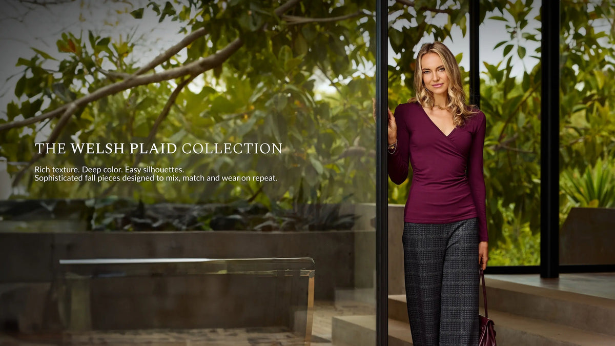 A woman stands by a glass door wearing a deep burgundy long-sleeve top and dark gray plaid trousers, with outdoor greenery visible behind her. Text on the left reads 'THE WELSH PLAID COLLECTION' with descriptive copy.