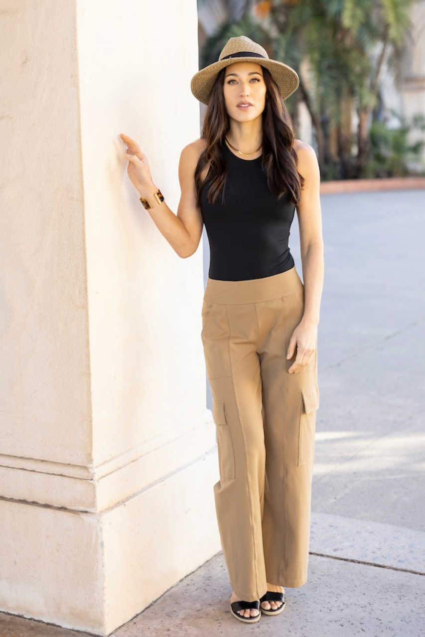 Full length photo of a woman wearing beige cargo wide leg pants and a black tank top and a beige straw hat