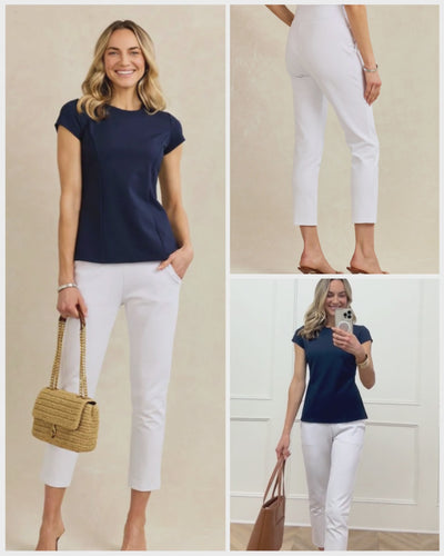 Video shows a women filming her outfit, navy blue short sleeve shirt and white trousers, in the mirror with a handbag.