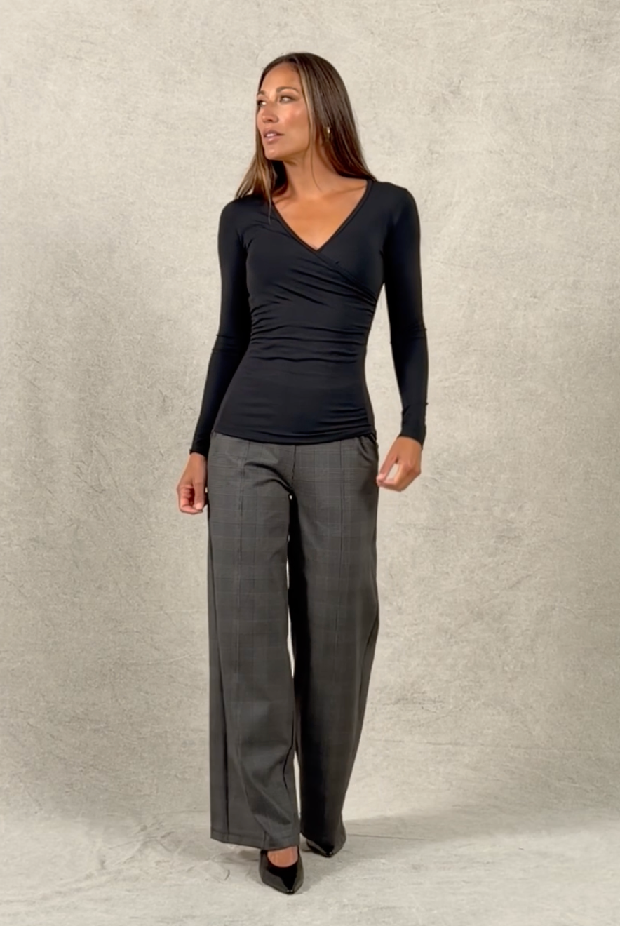 Woman walking on and off studio wearing plaid wide leg pants and black ruched v neck top untucked