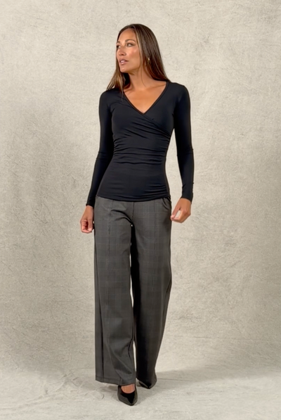 Woman walking on and off studio wearing plaid wide leg pants and black ruched v neck top untucked